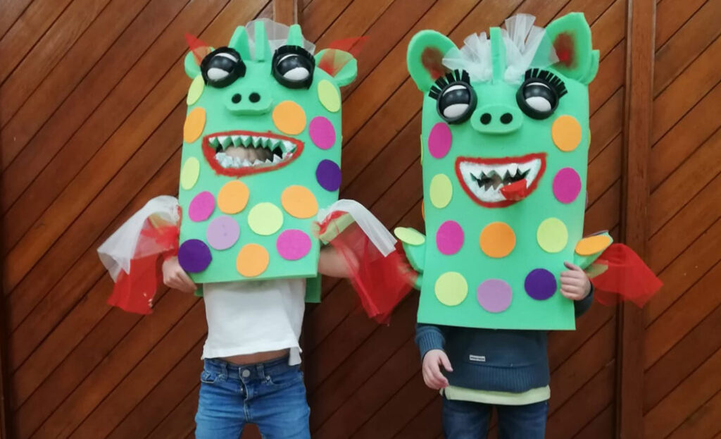 Disfraces con espuma de colores terminados, puestos por dos niños que agitan sus alas de tul rojo.